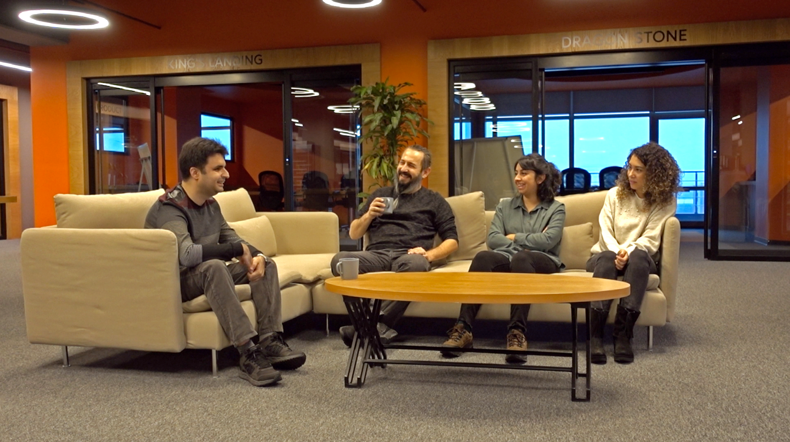 Four people happily sitting on sofas and drinking coffee next to a wooden coffee table with two more rooms in the background