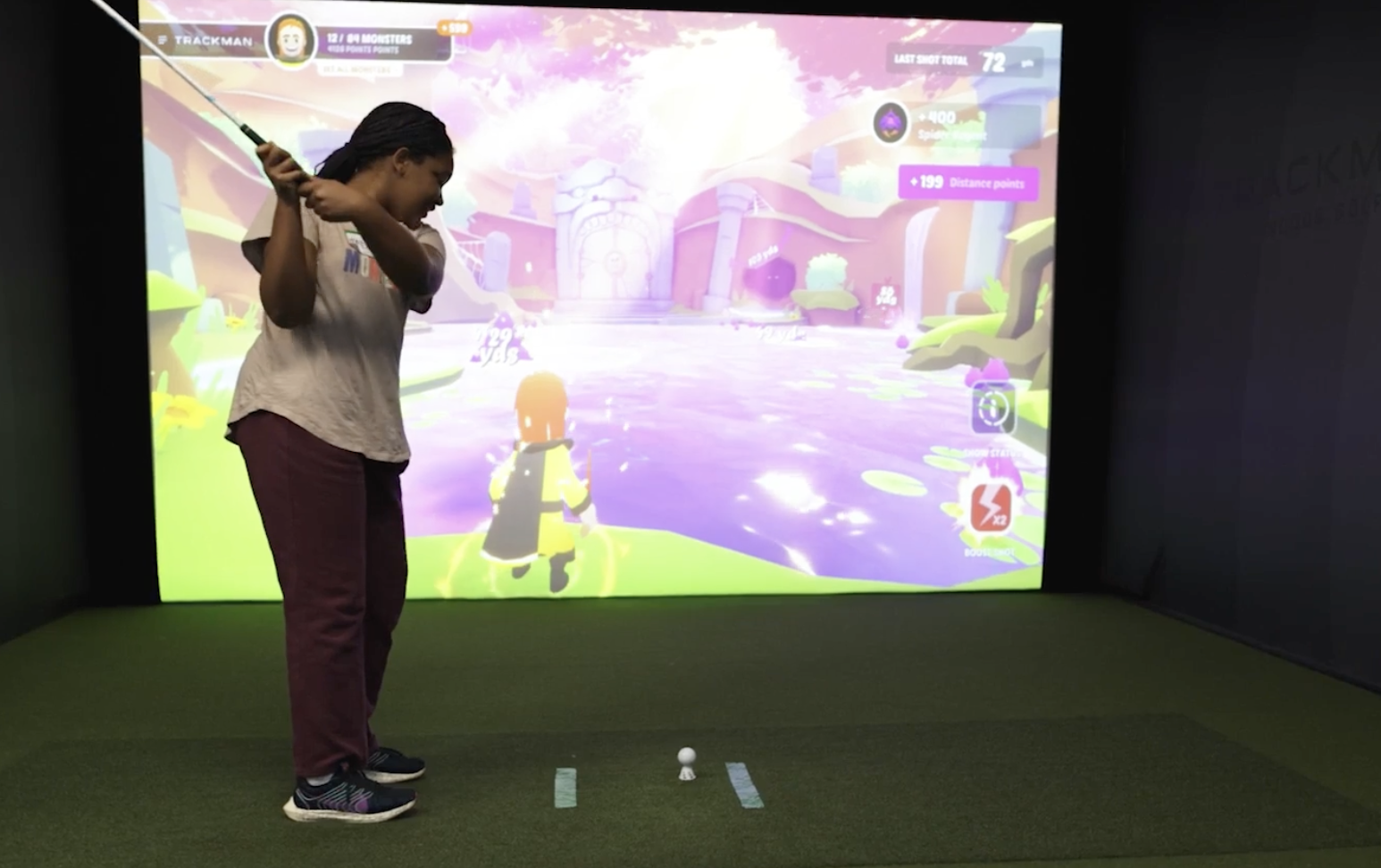 An individual playing virtual golf in an indoor simulator with a colorful on-screen course