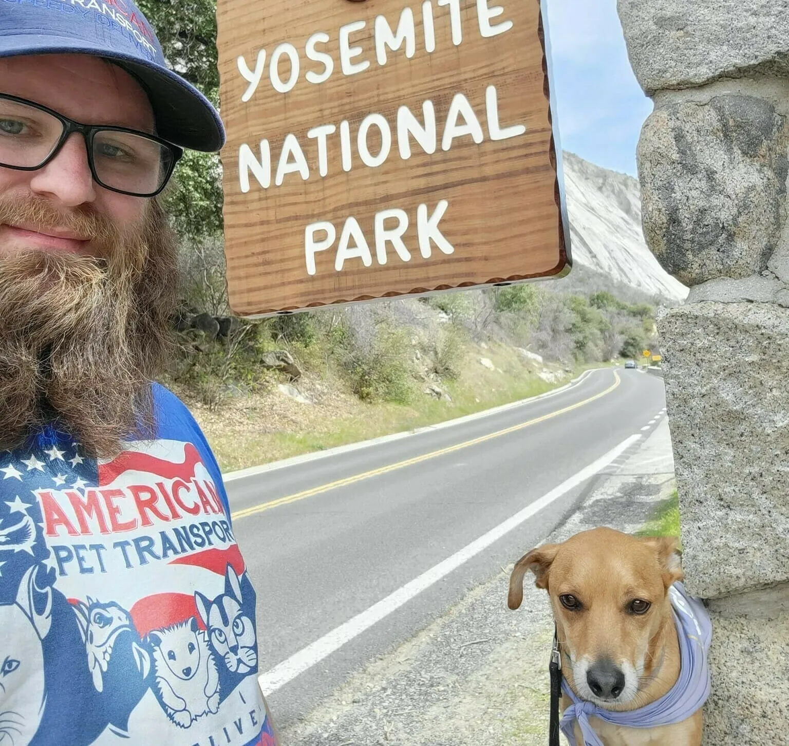 Man taking a selfie with his dog in front of the Yosemite National Park sign