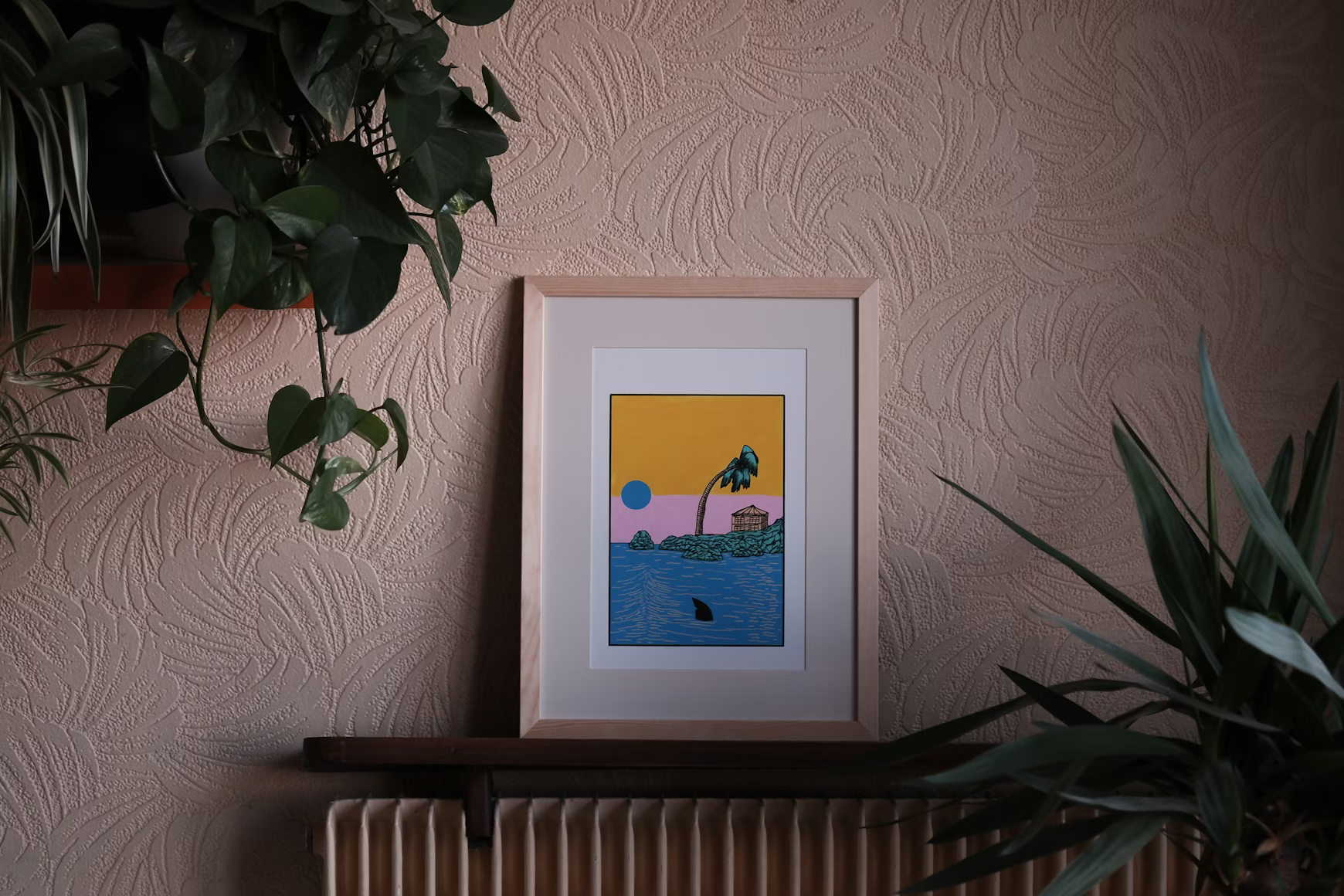 Framed wall art print displayed on a shelf between houseplants